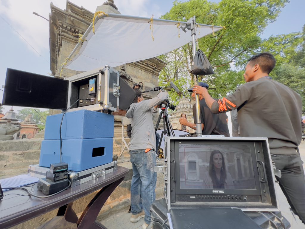 Film crew setting up a monitor and a reflector beside a stone temple in Nepal