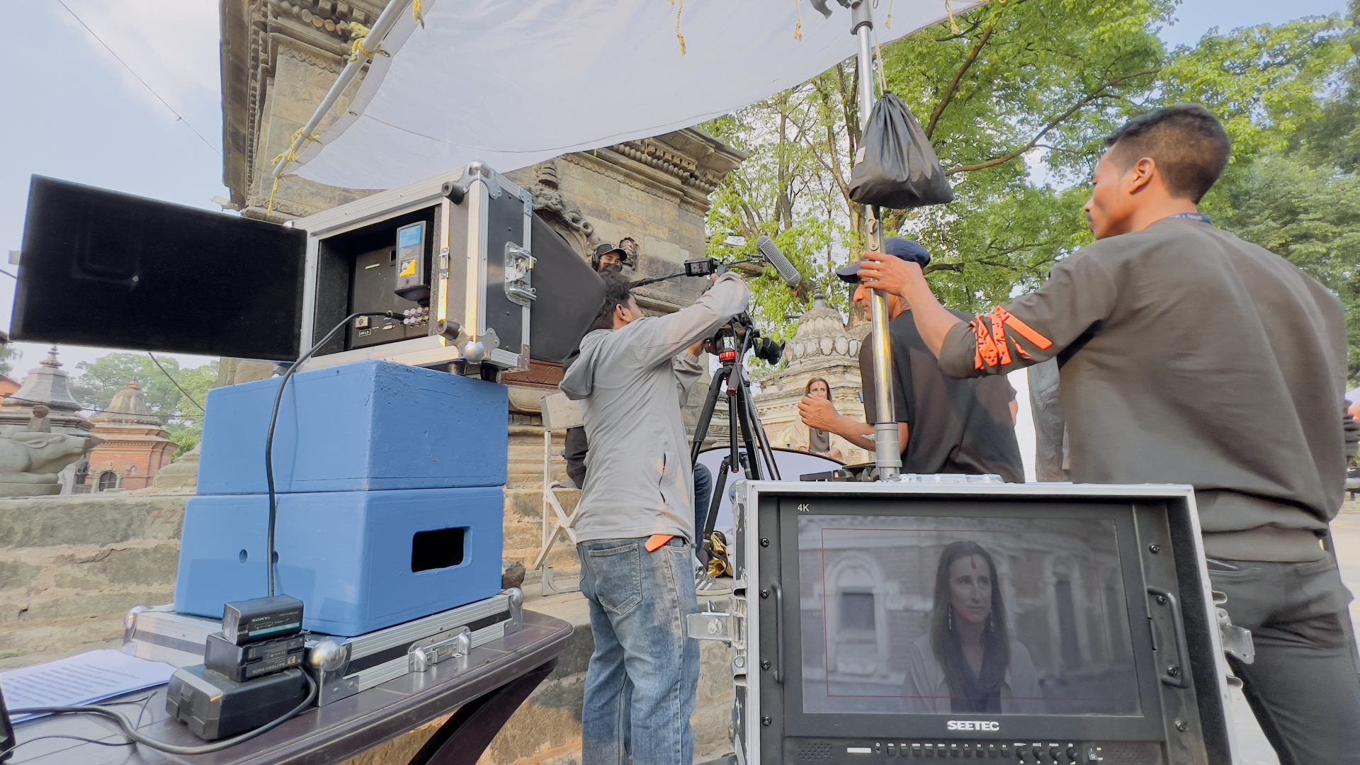 Film crew setting up a monitor and a reflector beside a stone temple in Nepal